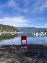 Red lifeguard chair on beach with houses on left and sailboats on right, Port Moody, North