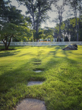 Residential front yard with stone pathway through green lawn to picket fence