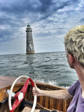 Young adult man driving vintage motor boat near lighthouse