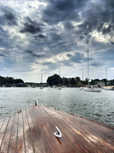 Bow of vintage wood boat with moored harbor sailboats in background