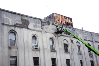 Workman repairing facade of old factory building, Brooklyn, NY, USA