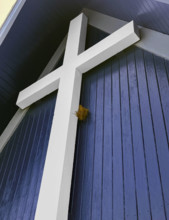 Bird nest tucked behind large white religious cross on building exterior, low angle view