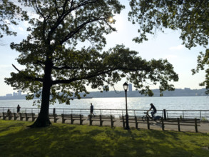 Joggers and bicyclist on westside bike path along Hudson River with view of New Jersey in background, Manhattan, New York City