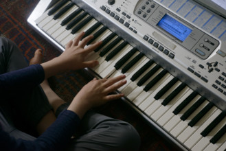 High angle view of young boy playing electric keyboard