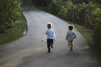 Rear view of two young boys running down paved driveway