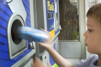 Young boy recycling cans in recycling bin