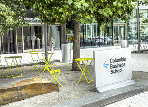 Sign and yellow bistro tables and chairs outside of David Geffen Hall, Columbia University Business