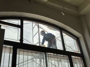 Construction worker repairing building façade, viewed through residential apartment window,