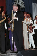 U.S. President Bill Clinton playing saxophone, as singer Dionne Warwick and others look on, at one