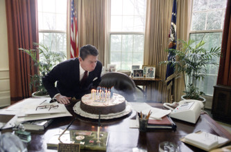 U.S. President Ronald Reagan blowing out candles on a cake while celebrating his birthday in Oval