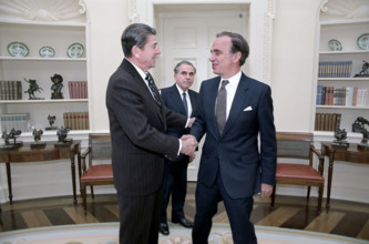 U.S. President Ronald Reagan shaking hands, with Rupert Murdoch as Director of U.S. Information