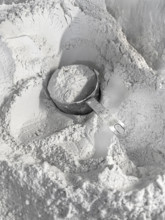 Full measuring cup of flour sitting in a mound of flour