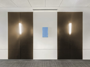 Two light fixtures mounted on hallway wall in office building