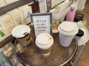 "Please leave drinks here" framed sign on round wood table with paper and plastic cups in retail