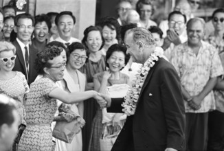 U.S. Vice President Lyndon B. Johnson wearing a lei and shaking a woman's hand, during an overnight