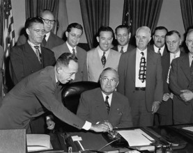 U.S. President Harry S. Truman seated at his desk preparing to push button activating a new