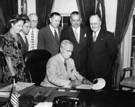U.S. President Harry S. Truman (seated) in the White House Oval Office signing bill to make