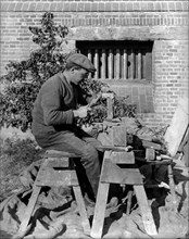 A craftsman shaping a brick on a bench at Great Dixter, Northiam, East Sussex, 1919