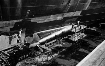 Men clean and paint the hull of a ship in the New Dry Dock, Tilbury Docks, Tilbury, c1945-c1965