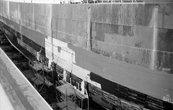 Men paint the hull of a ship in the New Dry Dock, Tilbury Docks, Tilbury, Essex, c1945-c1965