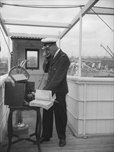 A ship's officer on the bridge uses a portable telephone connected to a land line, c1945-c1965