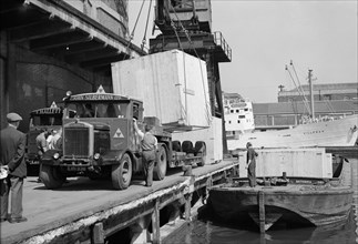 A large crate is hoisted from a lorry onto a barge at the West Quay, Wapping, London, c1945-c1965