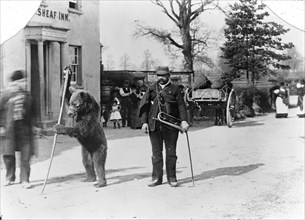 A dancing bear and owner performing outside an inn, Oxfordshire, c1900