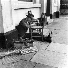 Man mending a chair on an East End street, London, 1950s. Artist: Henry Grant