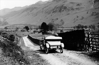 A vintage car travelling along a lane through the Lake District, Cumbria, 1920s. Artist: Unknown