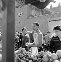 A woman buys fruit at a stall in a North London street market, c1946-c1959