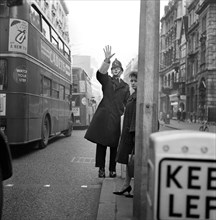 A policeman with his arm raised as two double decker buses pass by, City of London c1946-c1959