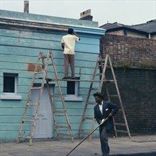 Man re-painting the exterior of a business premises in Kentish Town, London. 1960s