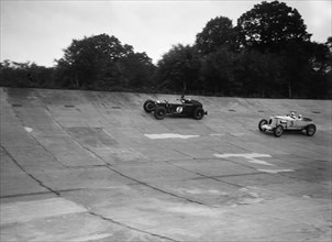 Invicta and Vauxhall 30/98 racing on the banking at an Inter-Club Meeting, Brooklands, 20 June 1931. Artist: Bill Brunell.
