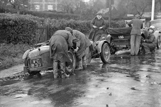 Attaching snow chains to JE Lancaster's Riley Brooklands during the Inter-Varsity Trial, 1930. Artist: Bill Brunell.