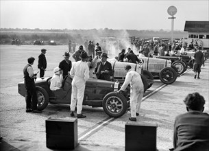 Cars on the start line, Surbiton Motor Club race meeting, Brooklands, Surrey, 1928. Artist: Bill Brunell.