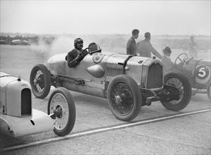 Riley, Buick and Bugatti on the start line at a Surbiton Motor Club race meeting, Brooklands, 1928. Artist: Bill Brunell.
