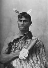 A Maori youth carrying the flat greenstone (nephrite) club known as a mere, 1902. Artist: Iles.