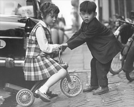 Children playing with a tricycle, c1960s.