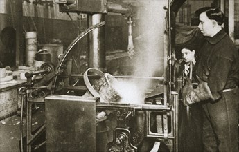 Making money; lowering a pot of liquid metal into a machine, 20th century. Artist: Unknown