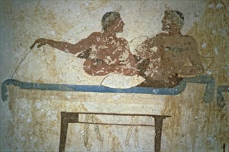Fresco depicting two men lying on a bed in the Tuffatore tomb at Paestum.