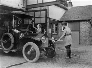 Chauffeuse washing car with hosepipe circa 1911. Creator: Unknown.