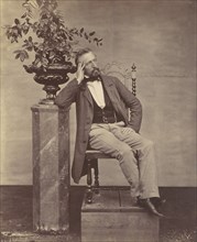 [Mathias Höusermann seated with elbow on pedestal holding a vase of flowers], 1850s-60s.