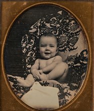 [Smiling, Nude Baby Holding Foot, Seated on Furniture Draped with Floral Print Fabric], 1850s.