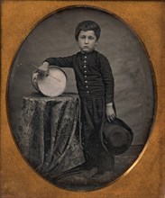Barefoot Boy Holding Hat and Drum Stick, Leaning Forearm on Child-sized Drum on Table, 1850s.