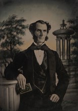 Man Holding Book, Standing Before a Painted Scenic Backdrop, 1850s-60s.