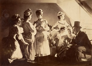 A Group of Six Costumed Women Posed in Interior with Top Hatted Gentlemen, c1885.