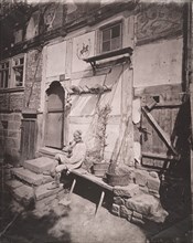 [Man Smoking Pipe Outside His Home on Village Street], 1880s.