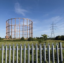 Leigh Road gas holder, East Ham, Newham, London, 2016. General view of the gasholder from the south, with a metal security fence in the foreground and an electricity pylon in the background.