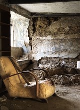 Interior view of the farmhouse, showing a ground-floor room with a collapsed cob wall, from the east, with a damaged old chair in the foreground, 2018.