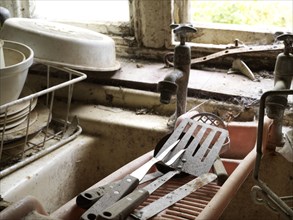 Bunksland Farmhouse, East Anstey, Devon, 2018. Detail of the sink in the kitchen on the ground-floor of the farmhouse, with disused cutlery and crockery abandoned on the drying rack.